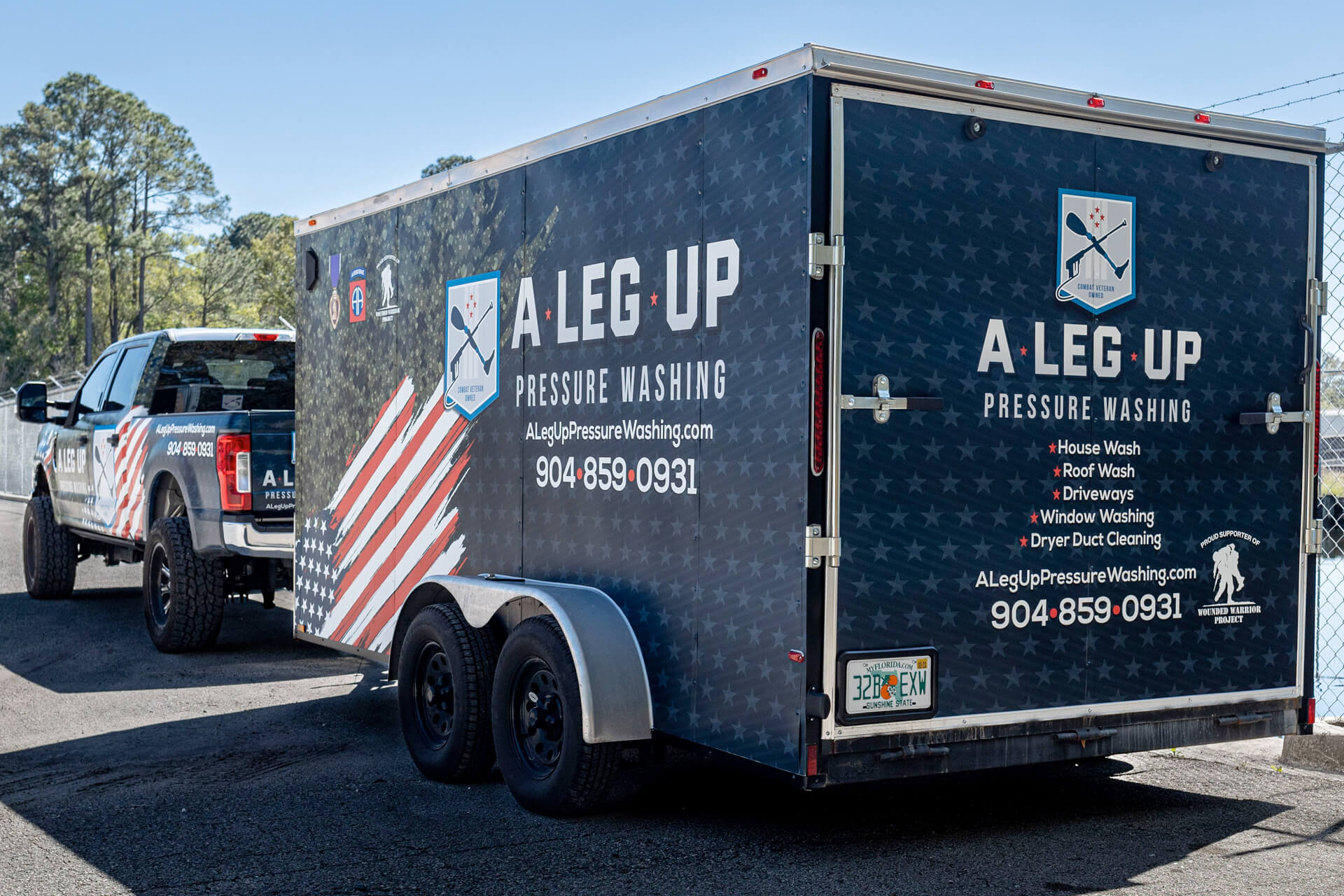 A blue cargo trailer with an American flag and local business graphics.
