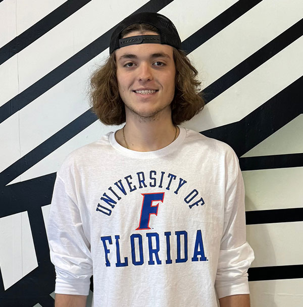 young man with longer brown hair, a backwards black hat, and a long sleeve white university of florida shirt